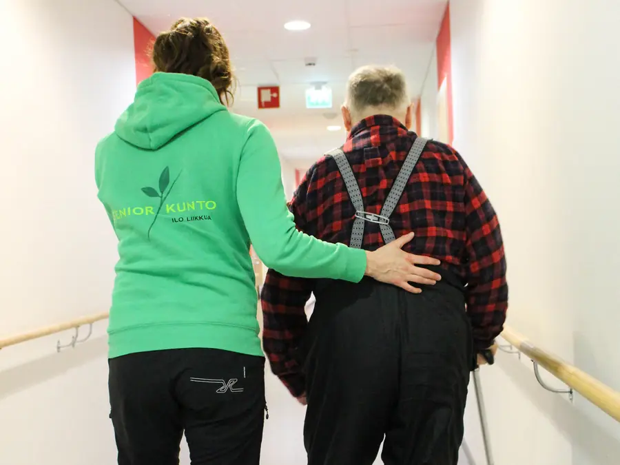 Fysioterapeutti tukee kävelevää asiakasta selästä